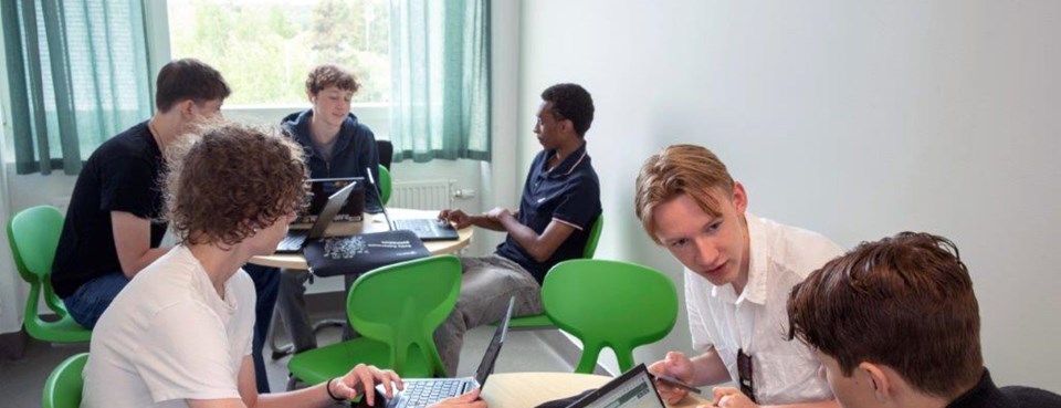 Elever vid runda bord pratar och studerar framför datorer