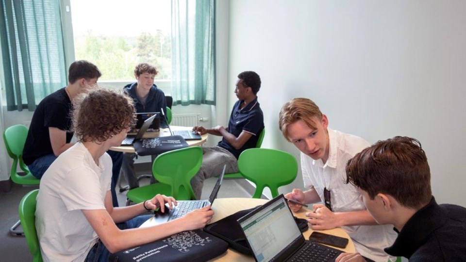 Elever vid runda bord pratar och studerar framför datorer